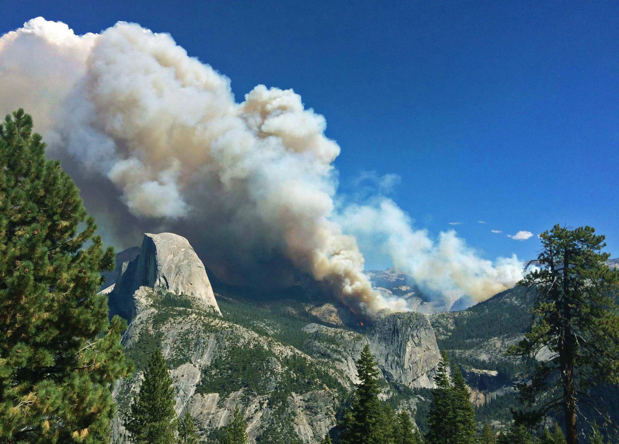 Smoke plume from wildfire with Half Dome and forested mountains in background