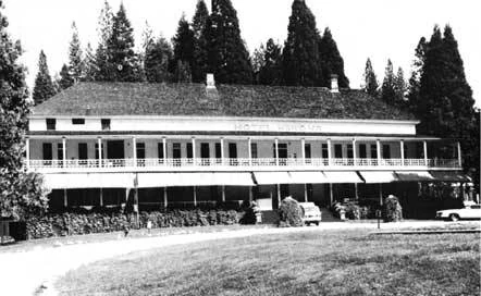 Black-and-white photograph of a large two-story hotel building with a porch and awnings, surrounded by trees and a grassy area.