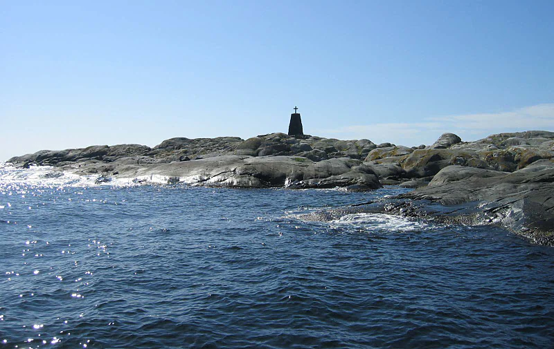 Rocky coastal landscape with water, tower structure on an island, clear blue sky