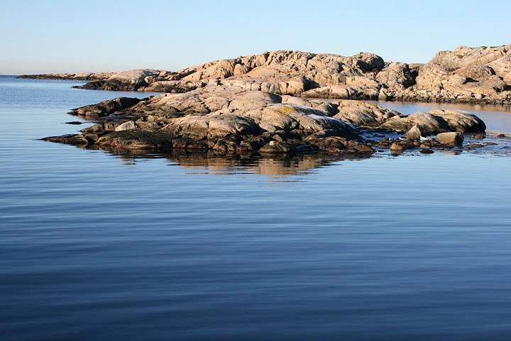 Calm blue water with rocky outcrops in the foreground and background under a clear sky